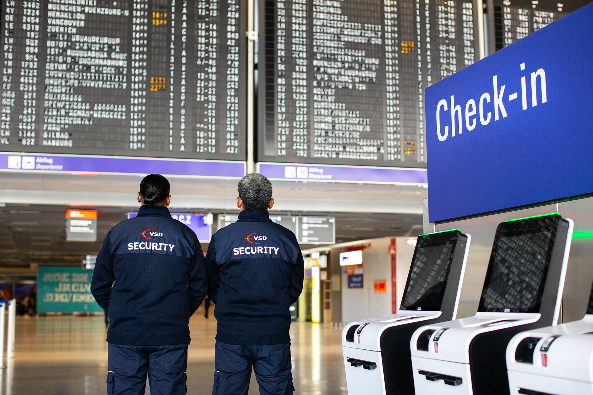 Zwei VSD Security Mitarbeiter im Check-in-Bereich des Flughafen Frankfurt vor der Abflugtafel – Aviation Security und Luftsicherheit am Frankfurt Airport