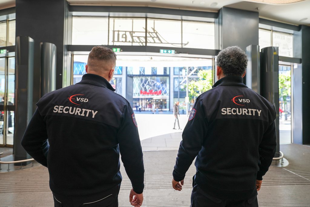 VSD Victory Sicherheitsdienste GmbH – zwei Security-Mitarbeiter beim Eingangsschutz eines Einzelhandelsgebäudes in der Frankfurter Zeil mit Blick auf die Einkaufsstraße